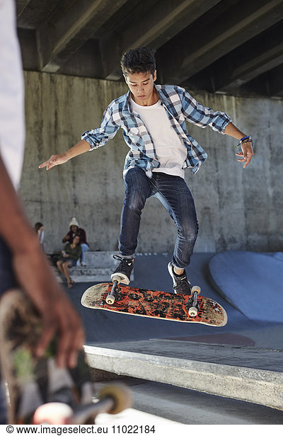 Focused teenage boy flipping skateboard at skate park