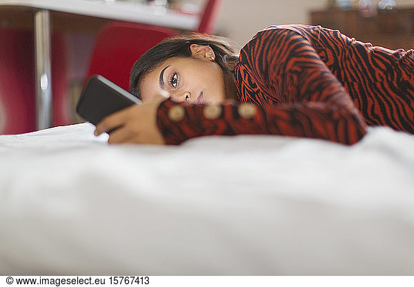 Focused teenage girl using smart phone laying on bed
