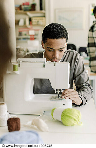 Focused teenage male student using sewing machine in art class at high school