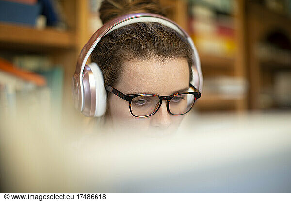 Focused woman with headphones and eyeglasses working from home