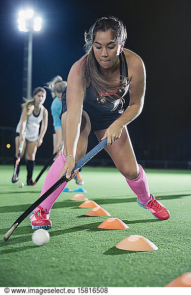 Focused young female field hockey player practicing sports drill on field