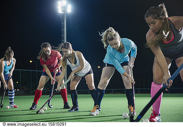 Focused young female field hockey players practicing sports drill on field at night