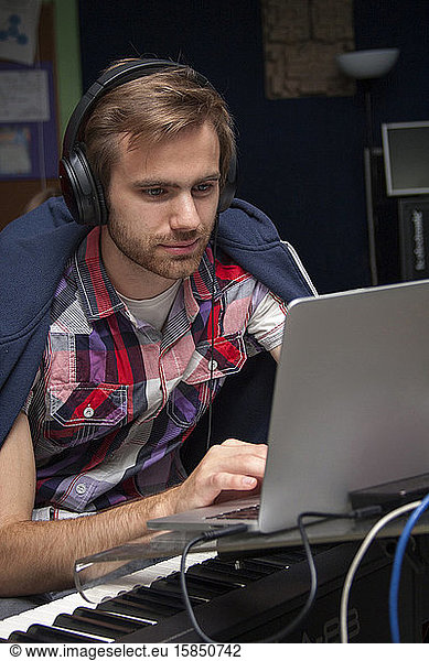 Focused young man in headphones composing on a laptop  piano  keyboard