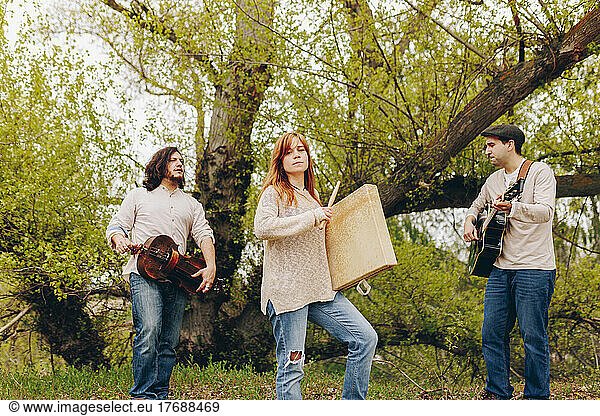 Folk music group doing rehearsal with musical instruments standing in front of tree