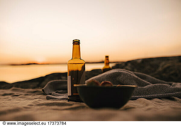 Food bowl and beer bottle at lakeshore during sunset