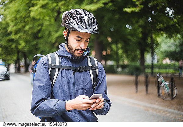 Food delivery man using mobile phone on street in city