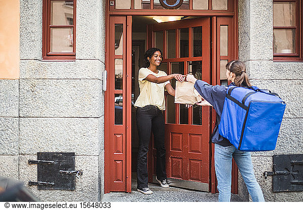Food delivery woman delivering package to customer standing at doorway in city