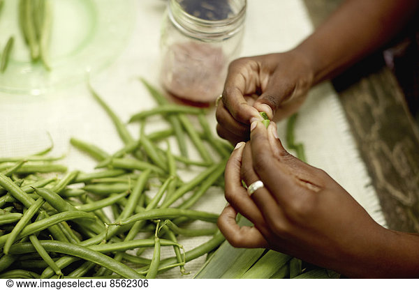 Food preparation outdoors. View onto a table  and a woman's hands preparing fresh green beans.