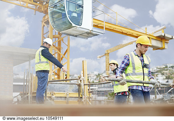Foreman guiding construction workers below crane at construction site