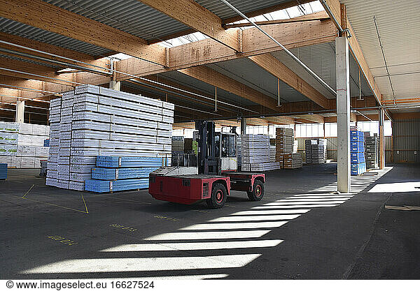 Forklift and stacked planks inside lumberyard warehouse