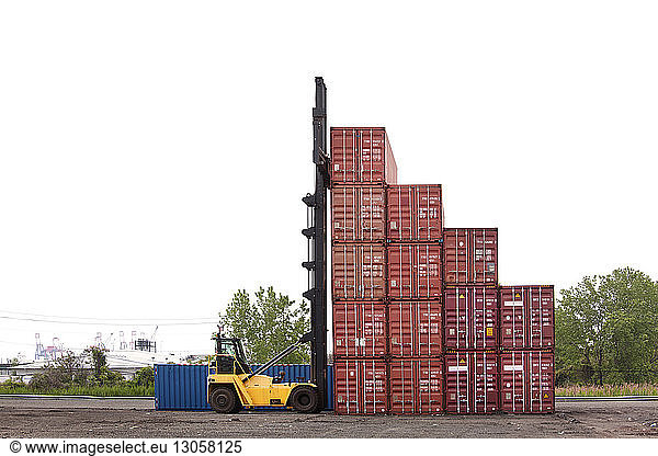 Forklift by cargo containers against clear sky