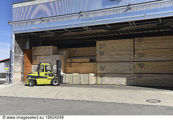 Forklift stacking planks inside lumberyard warehouse