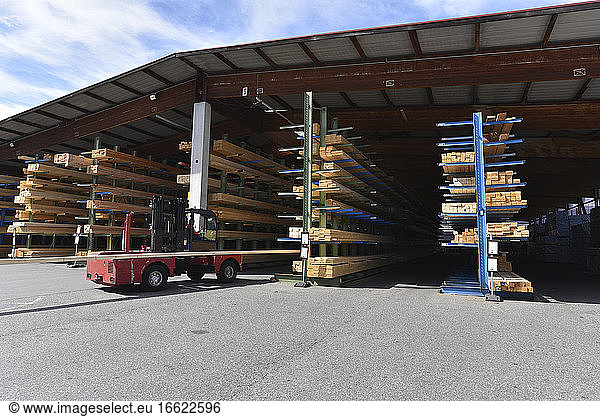 Forklift standing in front of planks stored on warehouse rack