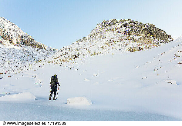 Forscher durchquert verschneite Landschaft in Richtung felsiger Berggipfel