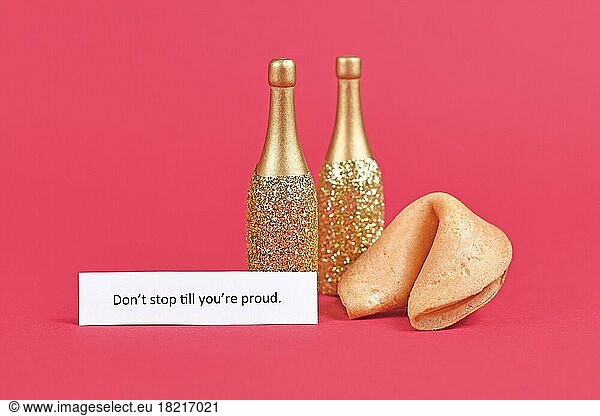 Fortune cookie and champagne bottles with motivational text 'Don't stop till you're proud' on paper on pink background