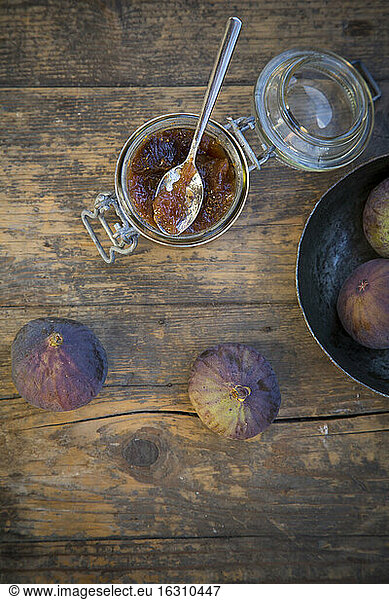 Four figs (Ficus carica) and a glass of fig jam on wooden table  studio shot