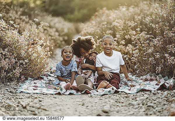 Four happy siblings sitting on blanket in flower field together