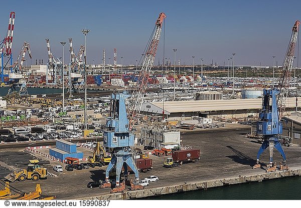Four-link cargo loading cranes on dock with parked motor vehicles ready for shipping plus container loading cranes in background  Ashdod Port  Israel.
