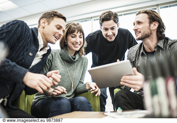 Four people colleagues at a meeting and one man sharing a tablet with the group.