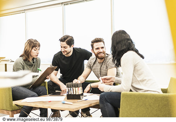 Four people  colleagues at a planning meeting holding coloured pens and working on paper and tablets.