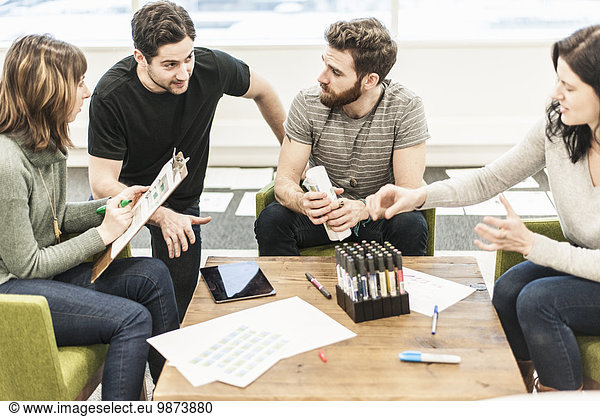 Four people seated at a table  colleagues at a planning meeting holding coloured pens and working on paper and tablets.