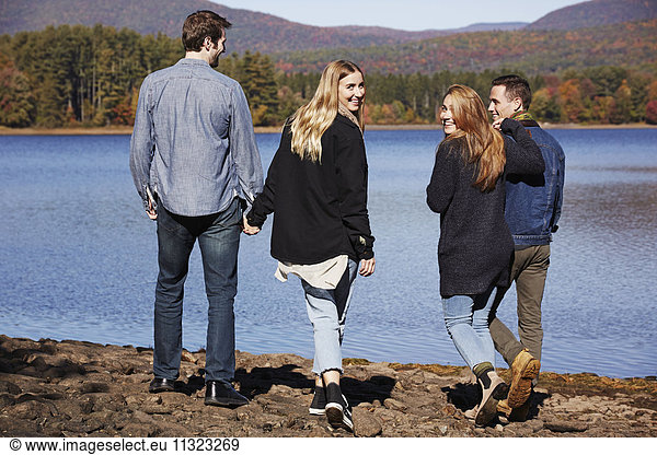 Four people walking along  couples hand in hand  on the shore of a lake.