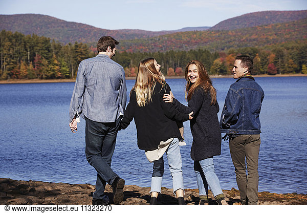 Four people walking along  couples hand in hand  on the shore of a lake.