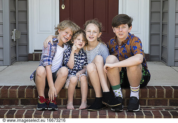 Four Siblings Sit Together on Brick Front Steps in Mismatched Outfits