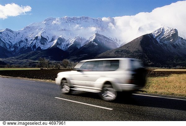 Four wheel drive car travelling along a road with snowcapped mountains in the background