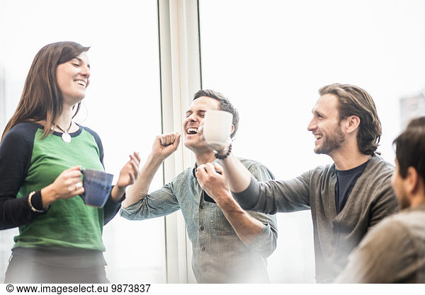 Four work colleagues on a break laughing and raising their coffee cups.