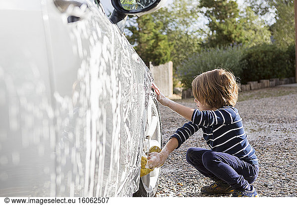 Four year old boy washing a car with cleaner and a cloth