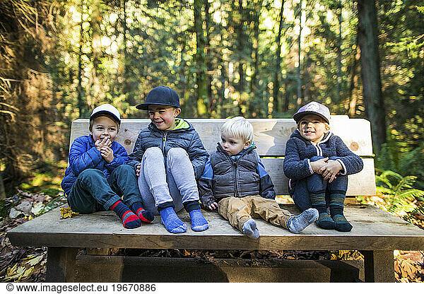 Four young kids sit  rest on wood park bench.