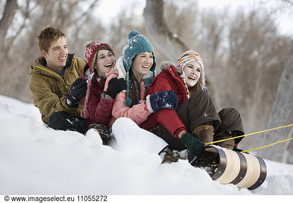 Four young people on a large sledge sliding across the snow  downhill.
