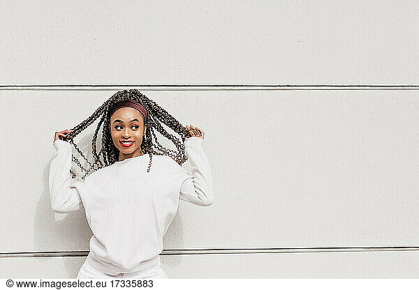 Fröhlich lächelnde Frau schaut weg  während sie vor einer weißen Wand steht