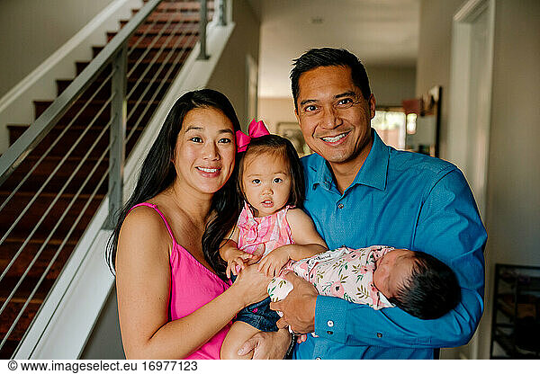 Fröhliche Familie mit Neugeborenem und 1 Jahr alter Tochter in modernem Haus