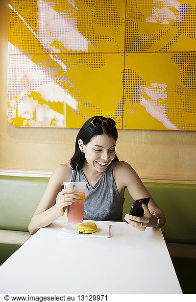 Fröhliche Frau benutzt Telefon während eines Drinks im Restaurant
