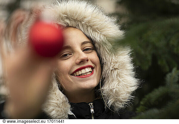 Fröhliche Frau in warmer Kleidung hält Weihnachtsschmuck bei kalten Temperaturen