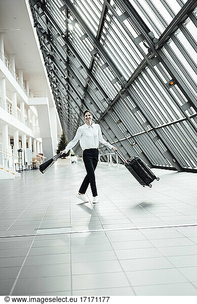 Fröhliche Frau mit Handtasche und Koffer auf einem Büroflur