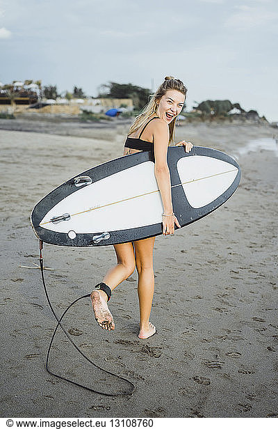 Fröhliche Frau trägt Surfbrett beim Strandspaziergang