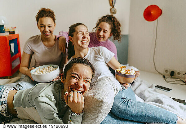 Fröhliche Freundinnen sehen fern  während sie zu Hause Snacks genießen