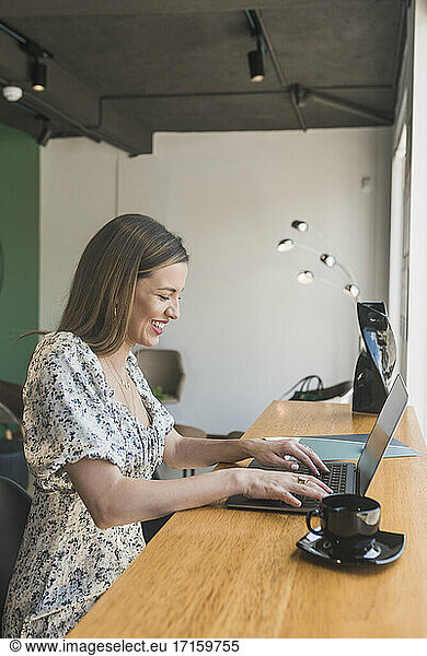 Fröhliche Geschäftsfrau arbeitet an einem Laptop auf einem Tisch in einem Café