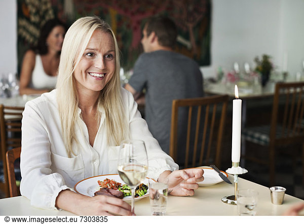 Fröhliche junge Frau am Restauranttisch mit Menschen im Hintergrund