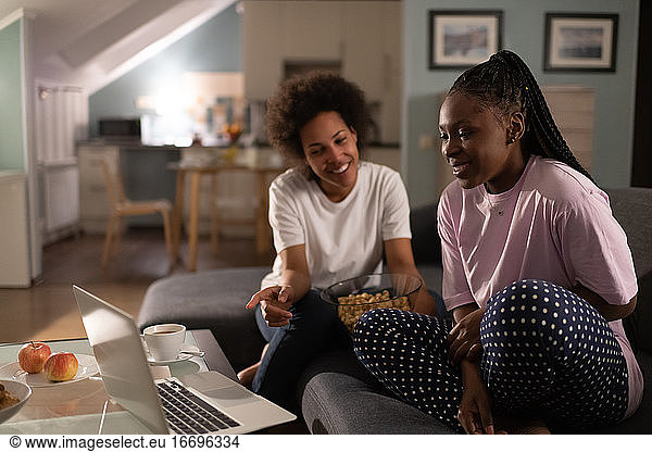 Fröhliche multiethnische Frauen diskutieren über einen Film  während sie auf ihren Laptop schauen