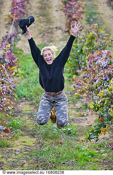 Fröhliche reife junge blonde Bäuerin springt in einem Weinberg Ackerland. Iguzkiza  Navarra  Spanien  Europa.