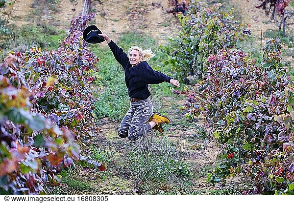 Fröhliche reife junge blonde Bäuerin springt in einem Weinberg Ackerland. Iguzkiza  Navarra  Spanien  Europa.