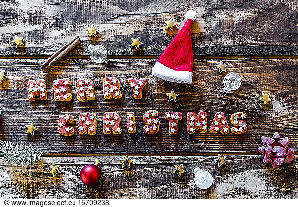 Fröhliche Weihnachten geschrieben mit Keksen und Weihnachtsdekoration auf Holzoberfläche