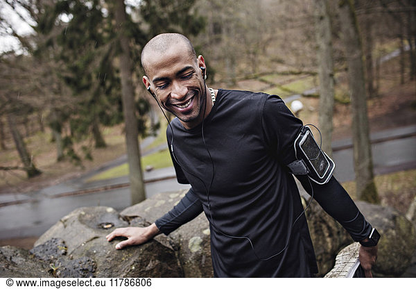 Fröhlicher Athlet  der Musik hört  während er an einer Steinmauer im Wald trainiert.