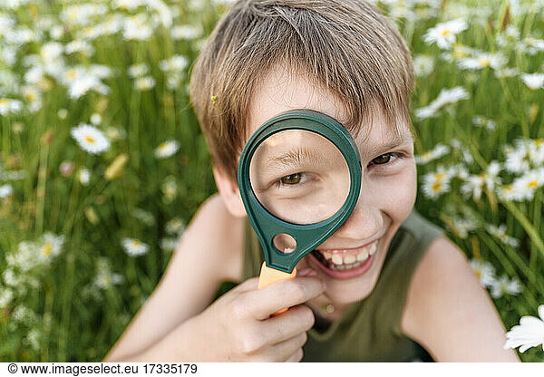 Fröhlicher Junge schaut durch ein Vergrößerungsglas in einem Feld