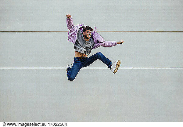 Fröhlicher Mann  der fröhlich gegen eine graue Wand springt
