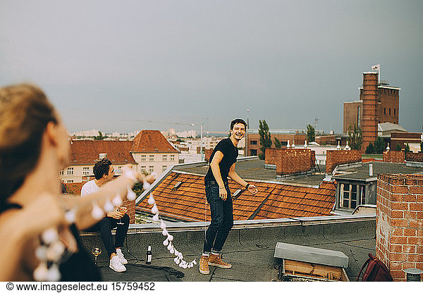 Fröhlicher Mann und fröhliche Frau spielen mit Streichlicht auf der Terrasse während einer Dachparty